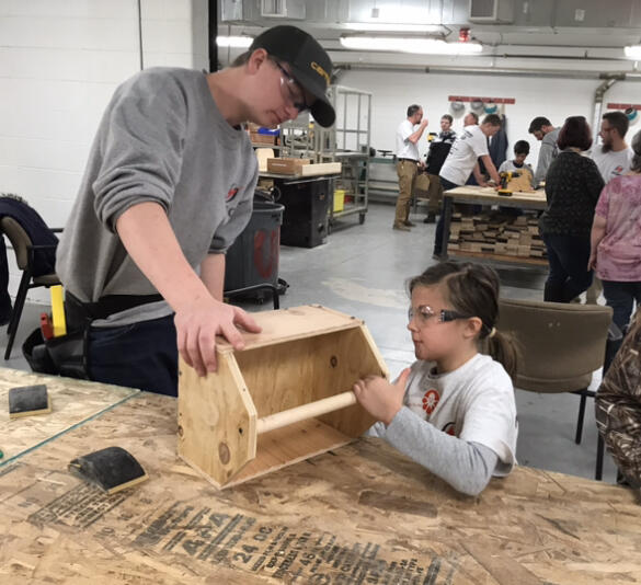 Child making a tool box with help of student